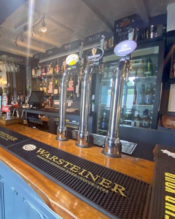 The bar at The Railway Inn, Lindal-in-Furness, with beer taps, a polished wooden counter and shelves of spirits